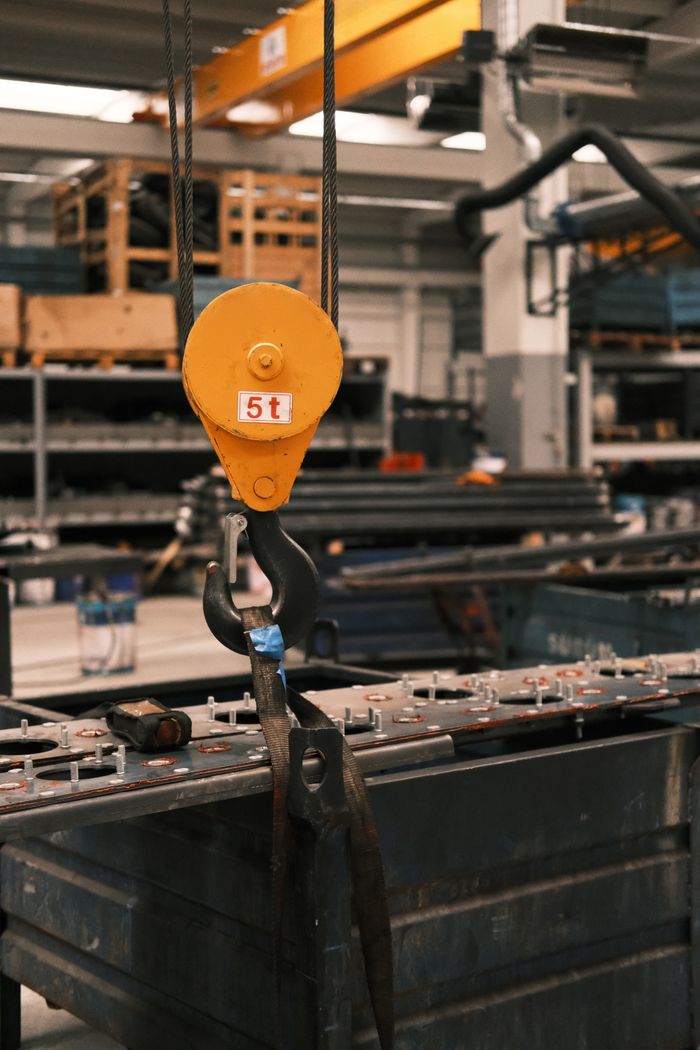 Yellow industrial hook lifting a 5-ton load in a factory setting.
